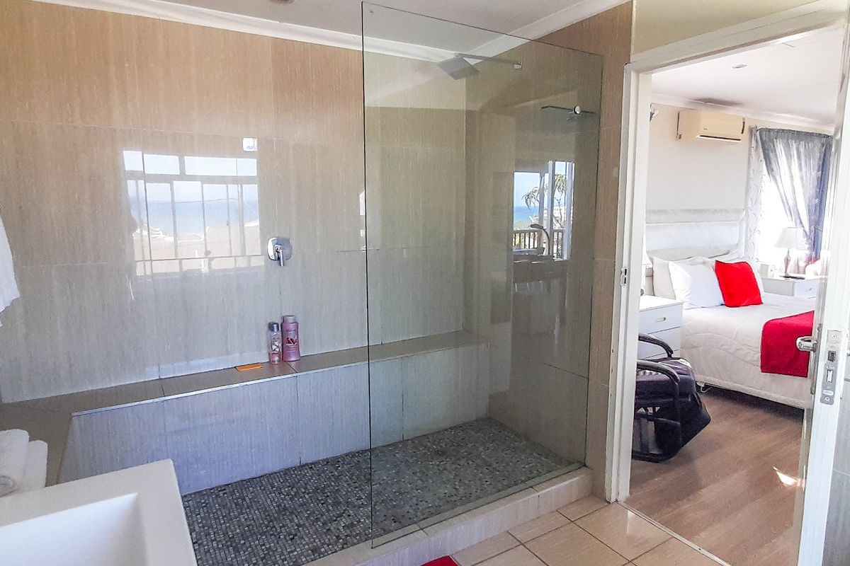 A modern bathroom featuring a spacious walk-in shower with a glass screen, pebble tile flooring, and a built-in bench, with views into the adjacent bedroom.
