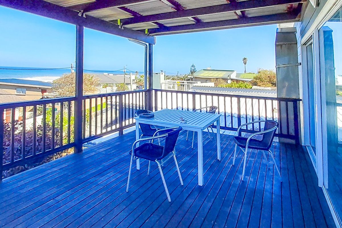 Spacious elevated balcony featuring timber decking, a protective roof covering, and a balustrade, offering expansive coastal views and direct access to the interior.