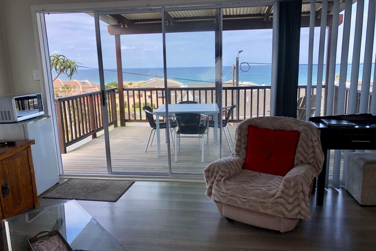Living area featuring large sliding glass doors that open onto a timber deck with ocean views.