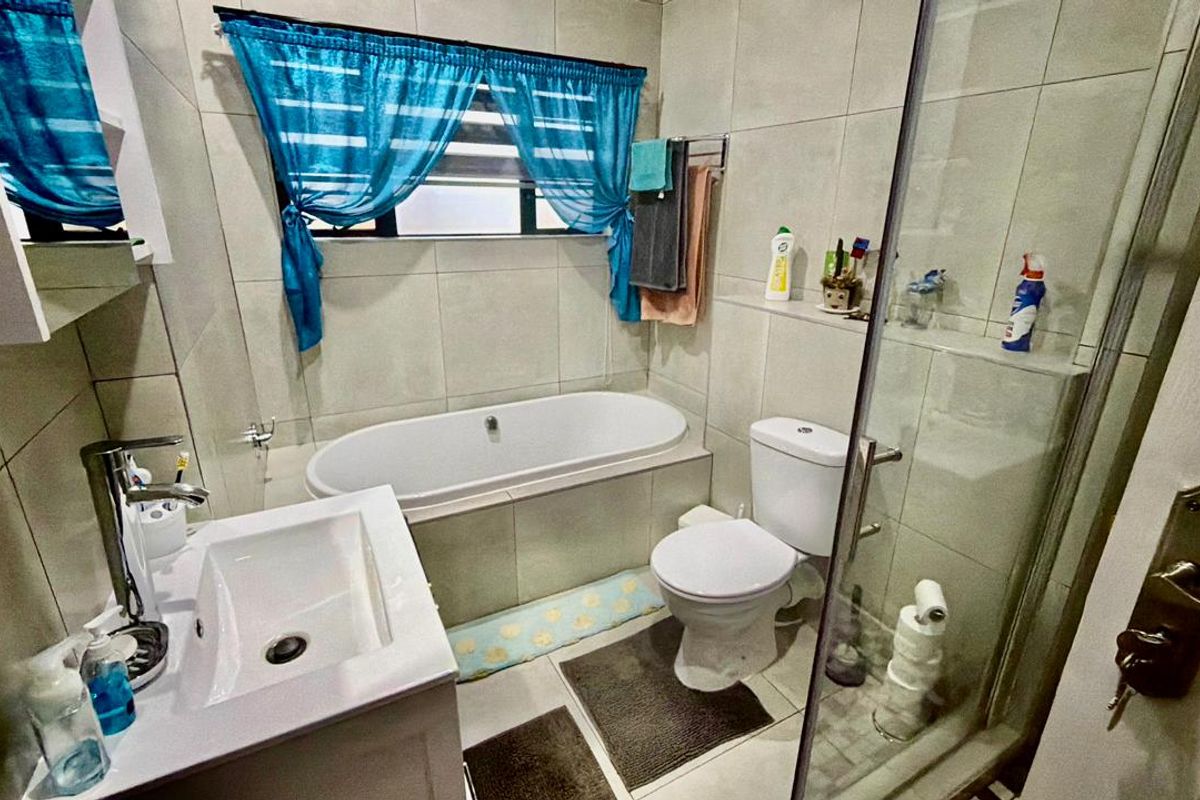 A functional bathroom featuring a built-in bathtub, a separate glass-enclosed shower, a vanity basin, and neutral wall tiling.