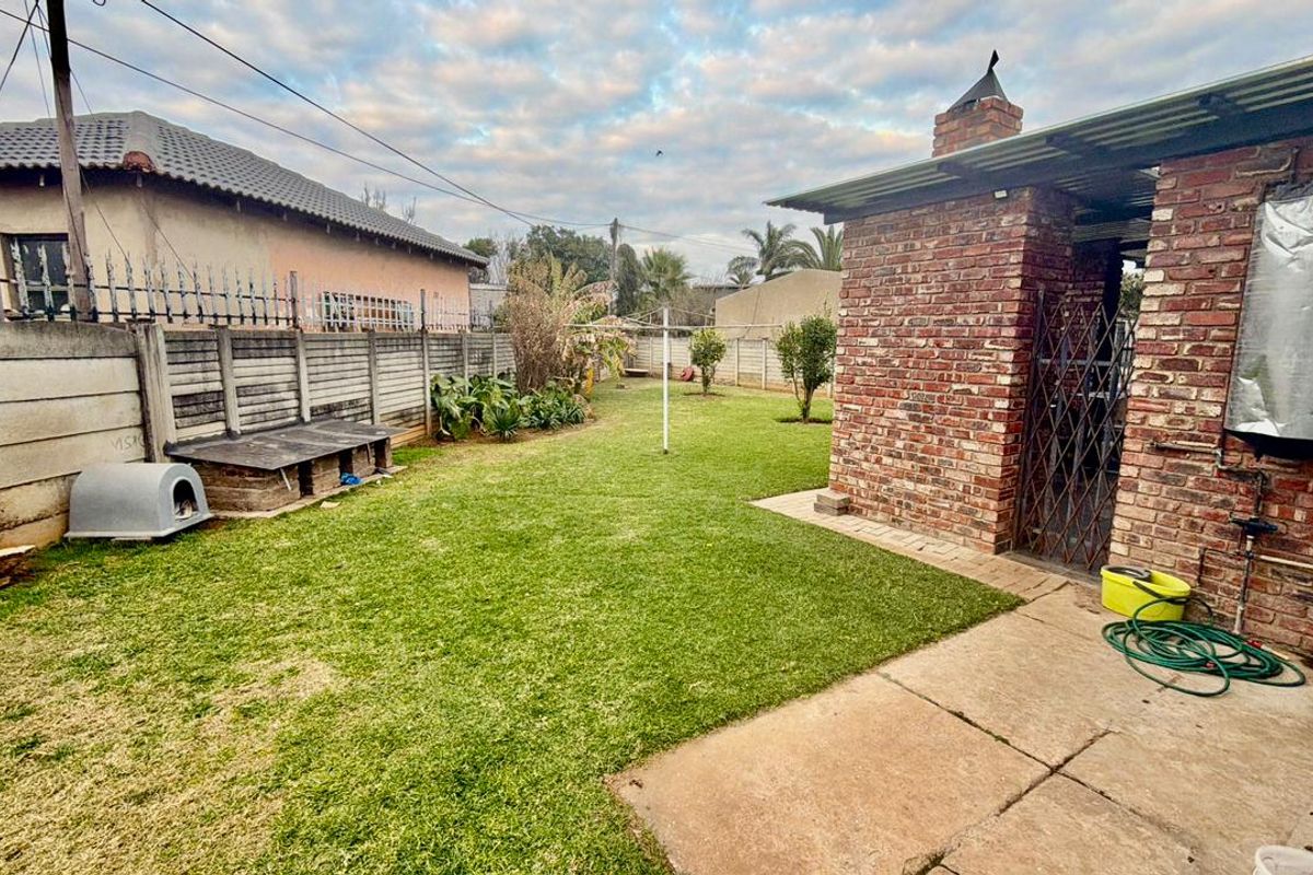 A rear garden featuring a lawn, paved patio area, and a brick structure with an external geyser and chimney.
