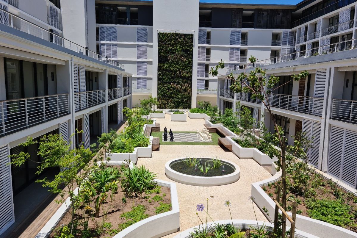 A well-maintained central courtyard featuring a vertical garden, water feature, paved walkways, and landscaped planters within a modern apartment complex.
