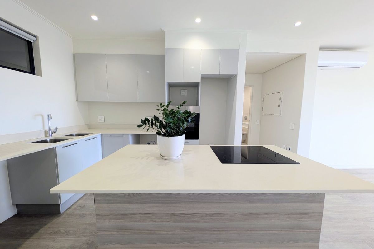 Modern kitchen featuring a central island with an integrated electric hob, sleek cabinetry, stainless steel sink, and recessed lighting in an open-plan layout.