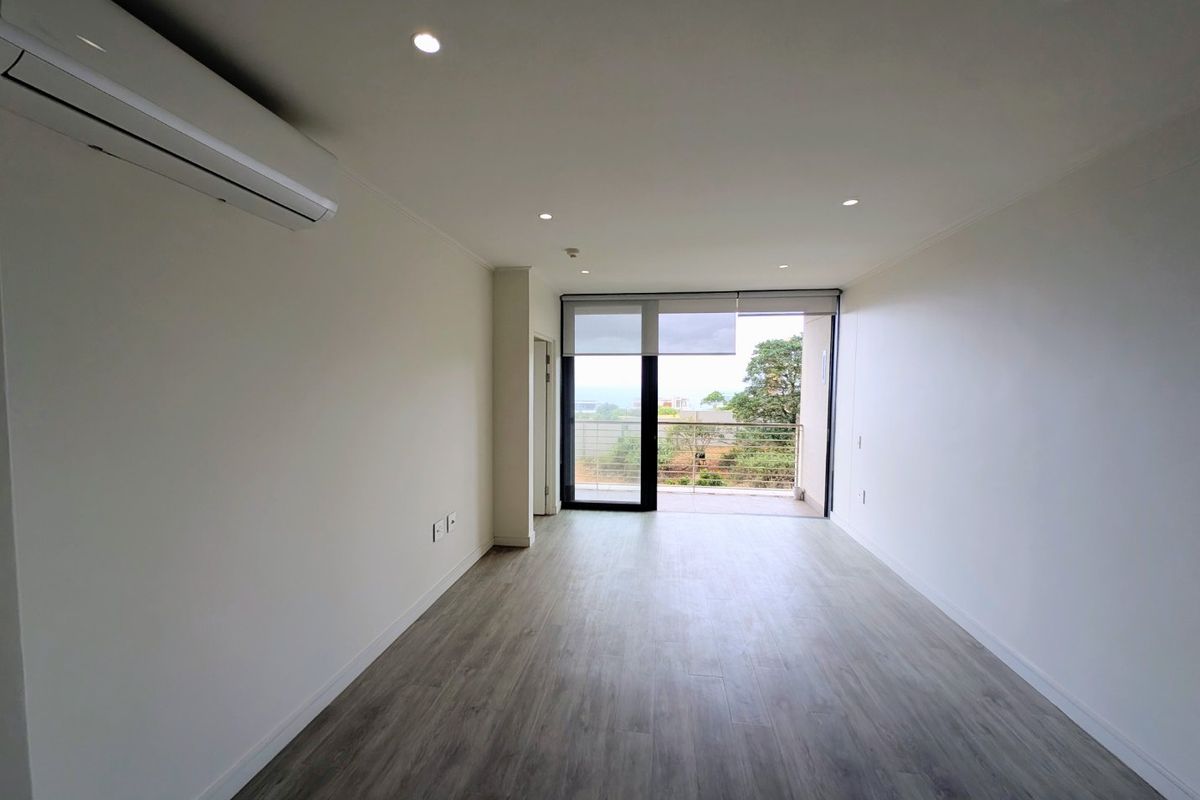 A bright, empty living area featuring modern wood-look flooring, recessed lighting, a split-system air conditioner, and direct access to a balcony.