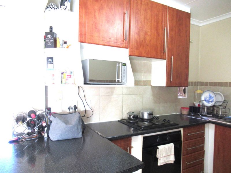 A functional kitchen featuring wood-finish cabinetry, dark granite countertops, a built-in oven, and an electric hob with a tiled backsplash.