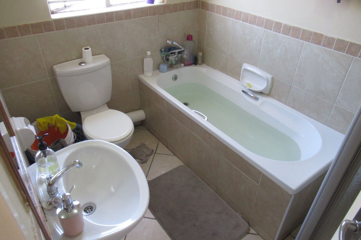 A functional bathroom featuring a pedestal basin, toilet, and a built-in bathtub with neutral wall and floor tiling.