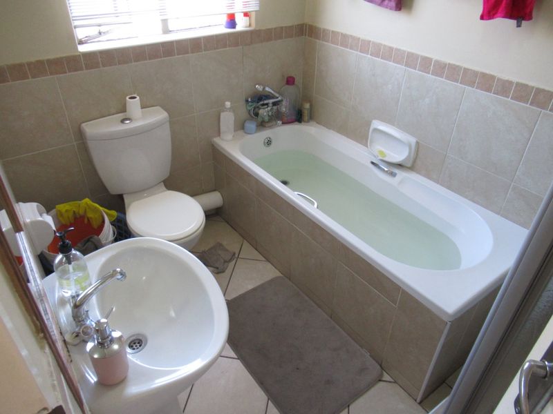 A functional bathroom featuring a pedestal basin, toilet, and a built-in bathtub with neutral wall and floor tiling.