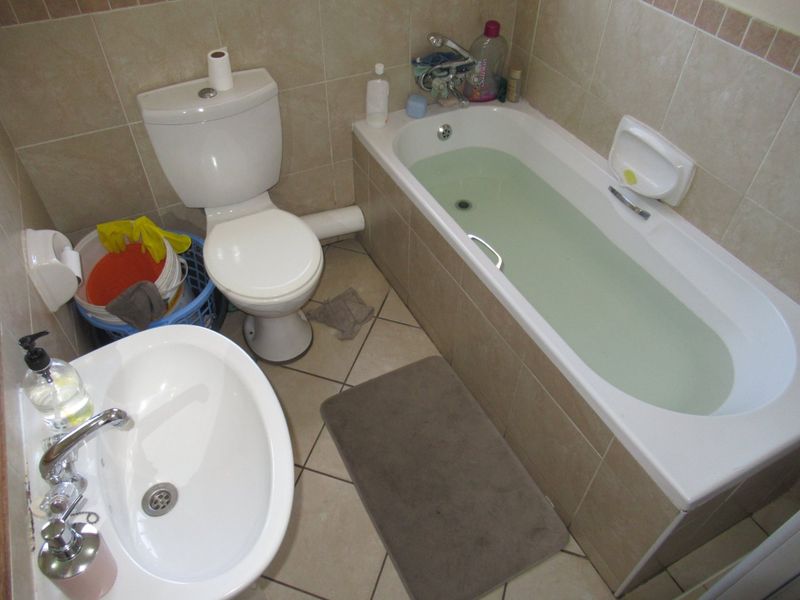 A functional bathroom featuring a bathtub, toilet, and pedestal basin with neutral wall and floor tiling.