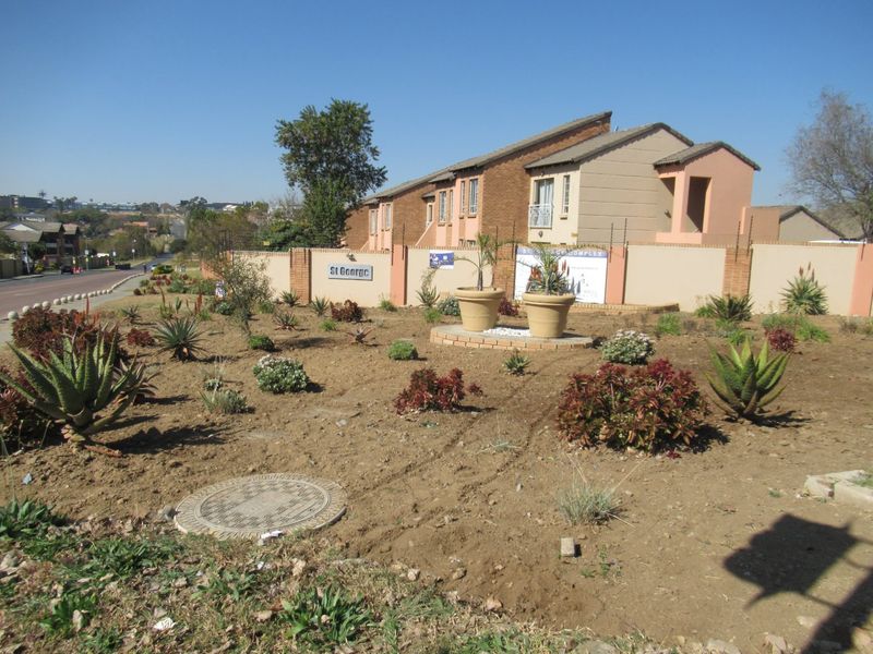 Exterior view of the St George apartment complex featuring a perimeter wall, electric fencing, and landscaped garden area with brick planters.