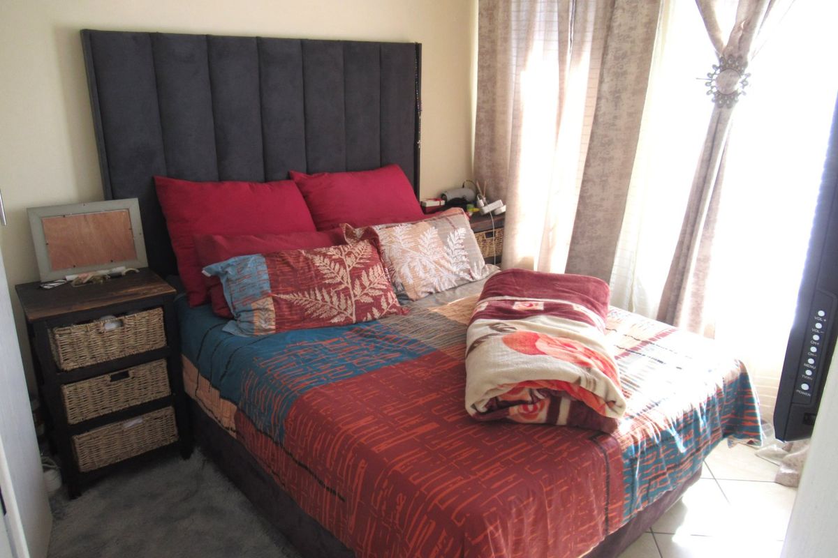 A cozy bedroom featuring tiled flooring and large windows with installed curtain tracks, providing natural light to the space.
