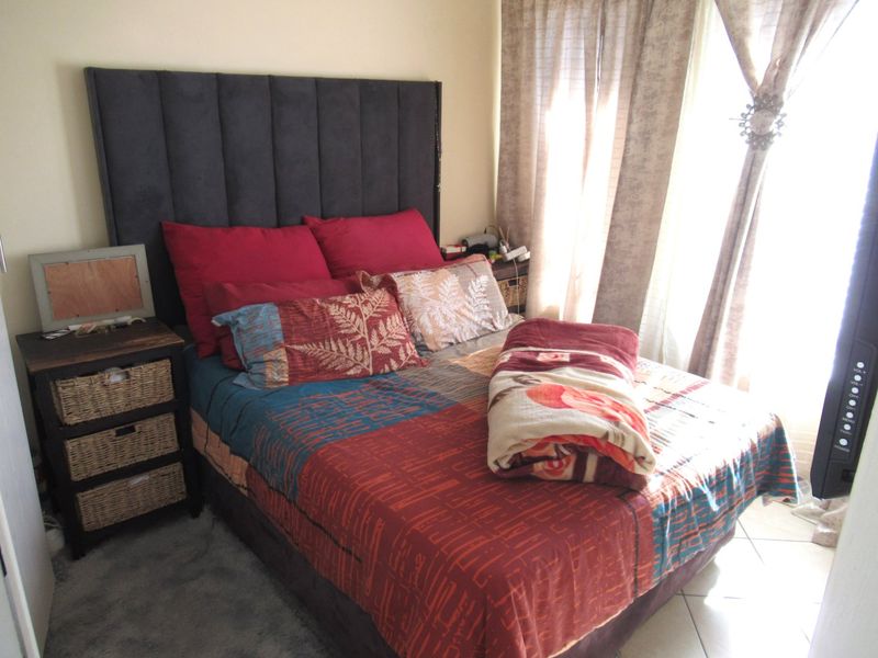 A cozy bedroom featuring tiled flooring and large windows with installed curtain tracks, providing natural light to the space.