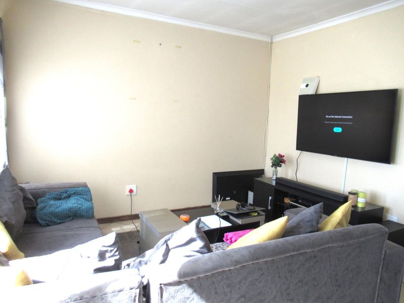 A living room area featuring coving and wall-mounted television, requiring minor cosmetic updates to the wall surfaces.