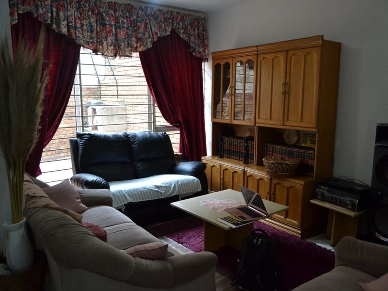 A living room area featuring a large window with security bars, providing natural light to the space.
