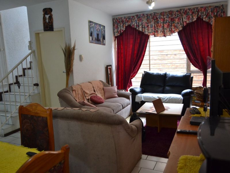A living room area featuring tiled flooring, a staircase with a security gate, and large windows fitted with security bars.