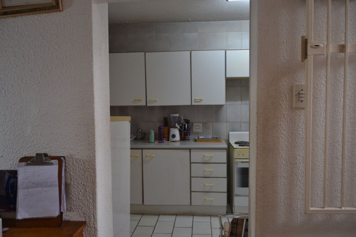 A compact, dated kitchen featuring white cabinetry, tiled backsplash, and tiled flooring, viewed through a doorway.