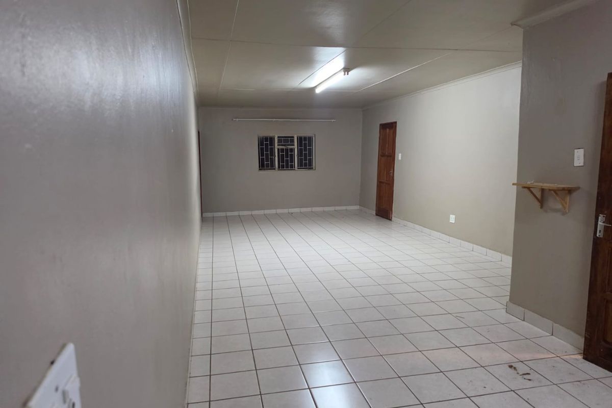 An empty, open-plan living area featuring neutral wall paint, tiled flooring, and a simple timber door, offering a blank canvas for interior design.