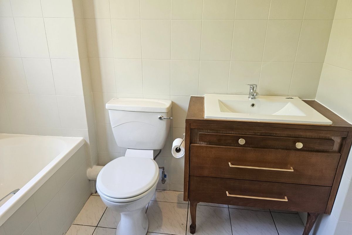 A functional bathroom featuring a built-in bathtub, a white ceramic toilet, and a wooden vanity cabinet with an integrated sink.