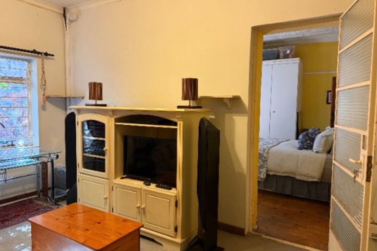 A living room area featuring a steel-framed window and a doorway leading to an adjacent bedroom with visible wear on the door frame.