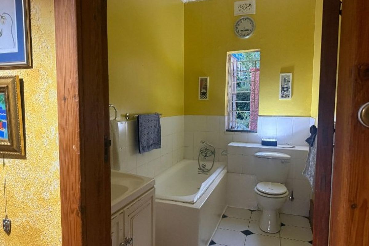A dated bathroom featuring a built-in bathtub, toilet, and vanity cabinet, with yellow wall paint and tiled finishes throughout.