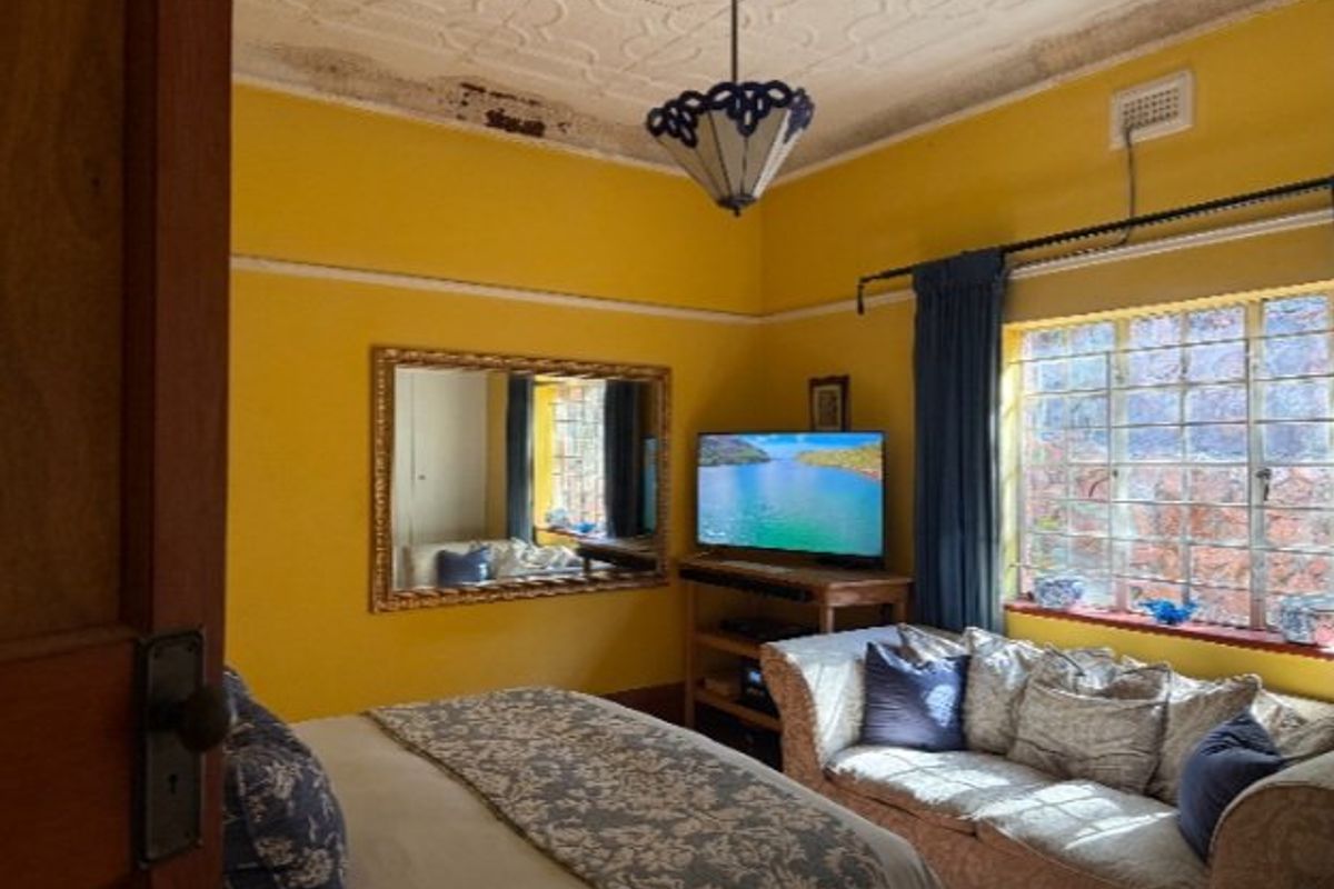 A bedroom featuring a decorative pressed metal ceiling, picture rails, and steel-framed windows, currently showing signs of ceiling wear and water staining.