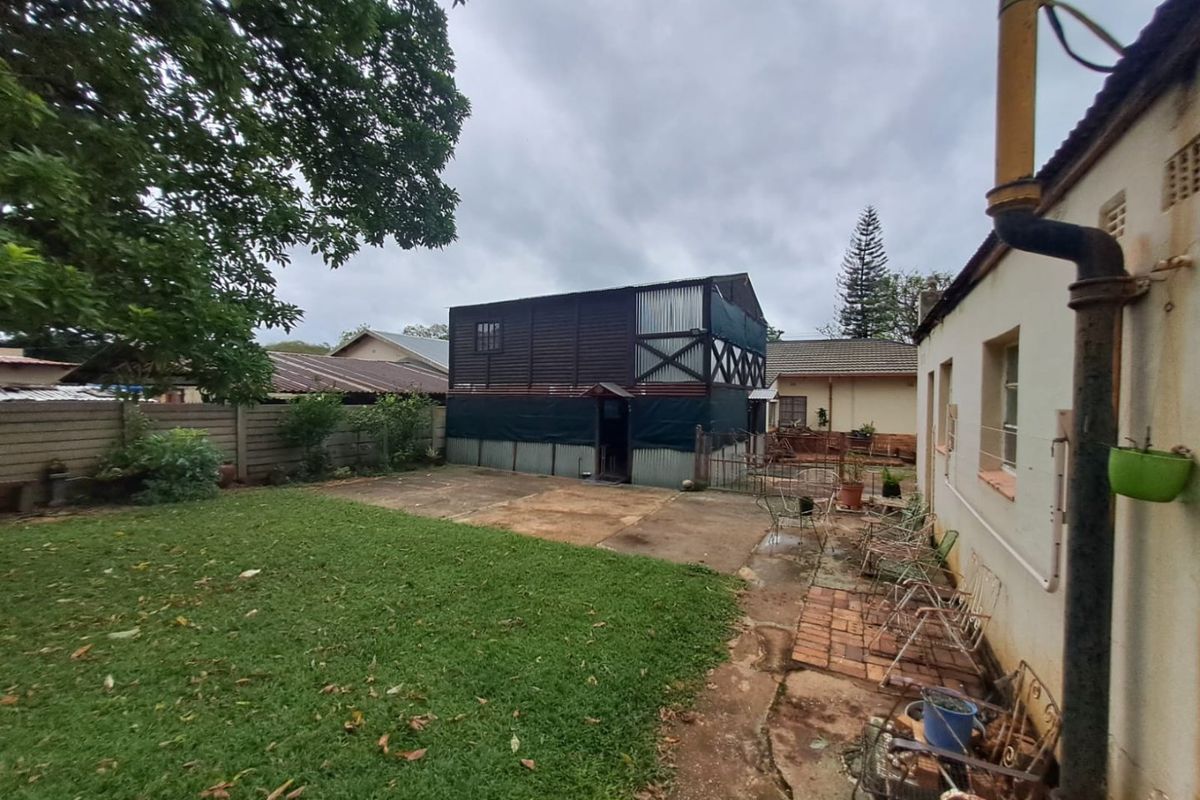 Rear garden area featuring a lawn, concrete paving, and a two-story outbuilding with timber and corrugated metal cladding.