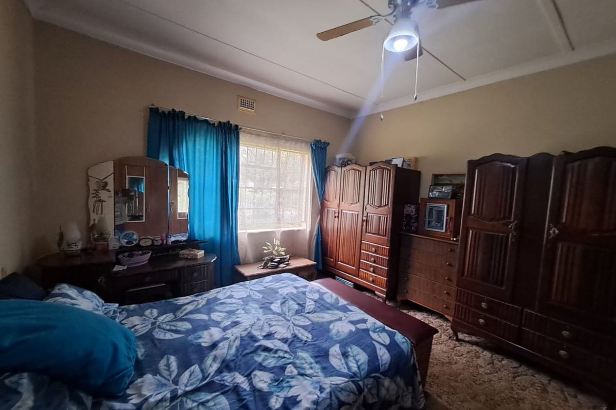 A bedroom featuring a ceiling fan and window, currently showing dated finishes and worn carpeting, offering potential for modernization and aesthetic improvement.