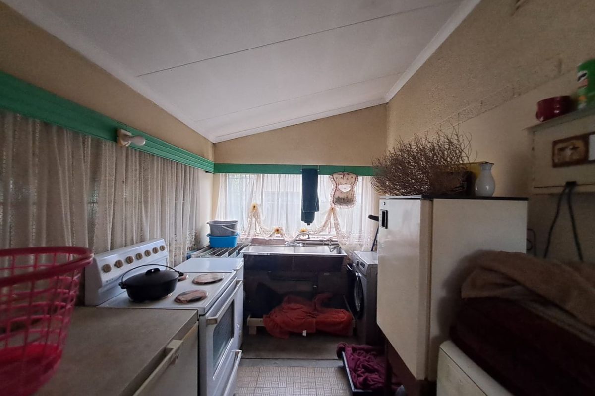 A dated kitchen area featuring a freestanding stove, double bowl sink, and tiled flooring, offering significant potential for modernization and renovation.