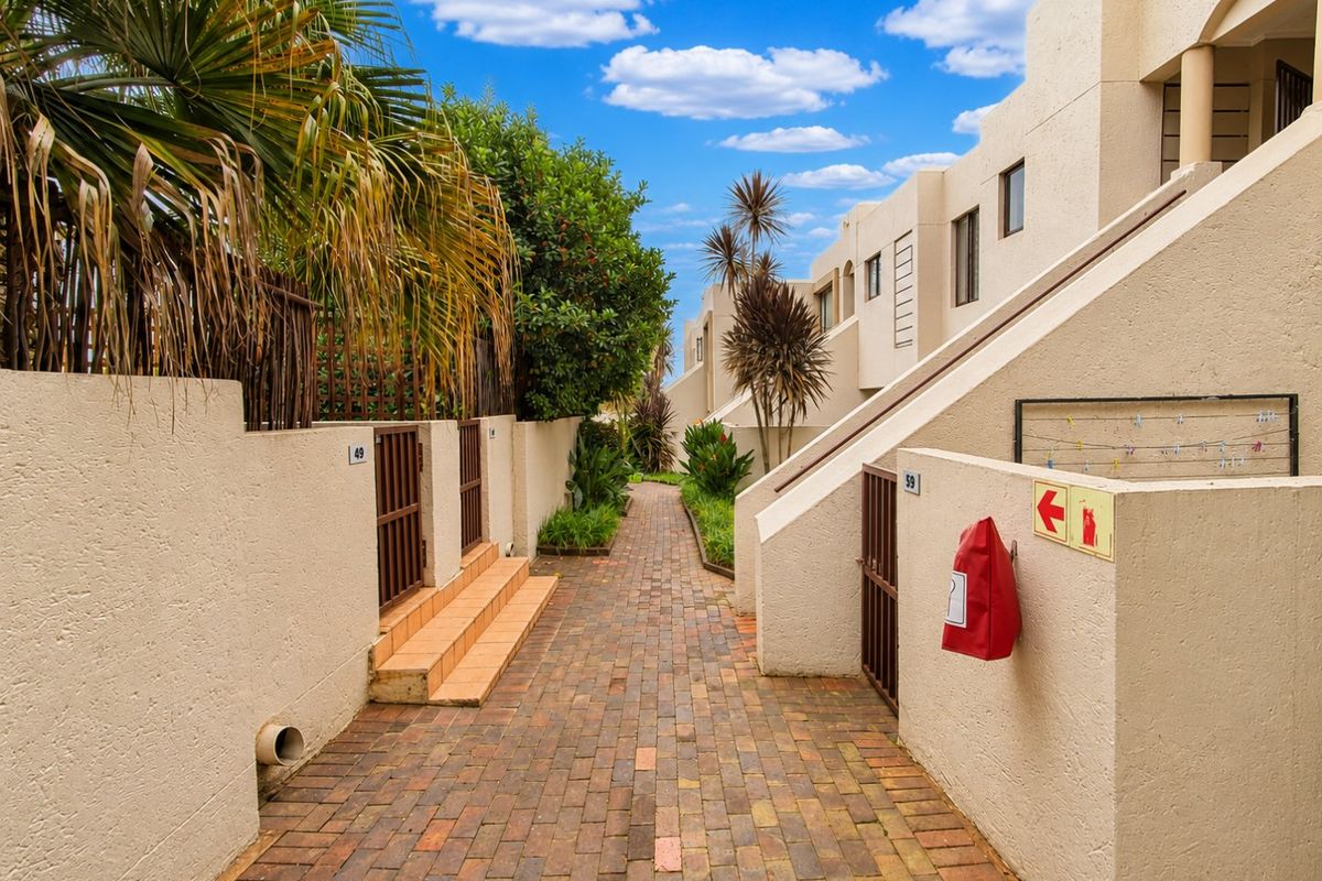 A well-maintained brick-paved walkway providing access between apartment units, featuring boundary walls, metal gates, and integrated fire safety equipment.