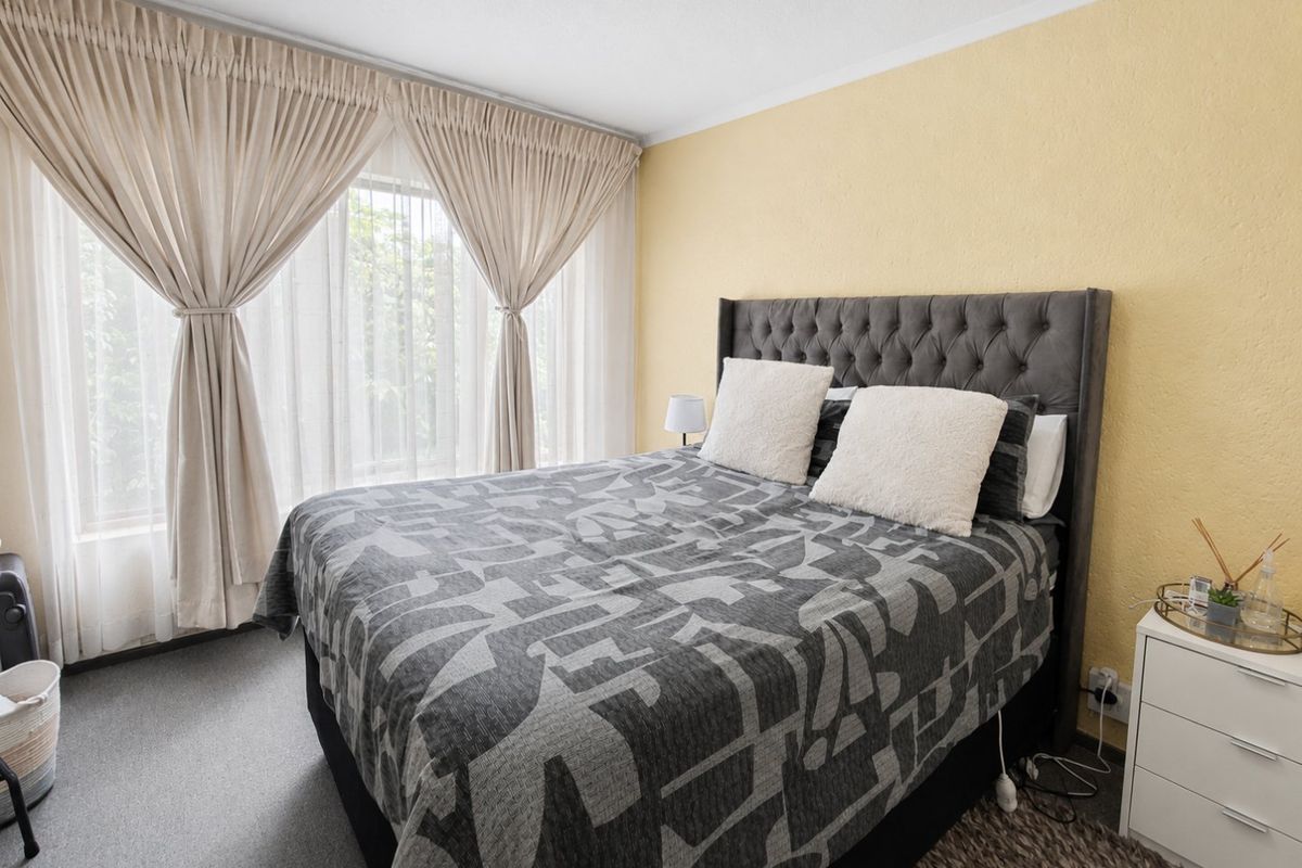A comfortable bedroom featuring neutral wall tones, carpeted flooring, and large windows with installed curtain tracks, providing a functional and well-lit living space.