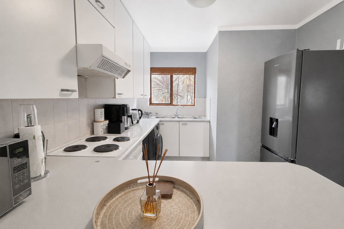 A functional kitchen featuring white cabinetry, an electric hob with extractor fan, double bowl sink, and tiled backsplash with neutral countertops.