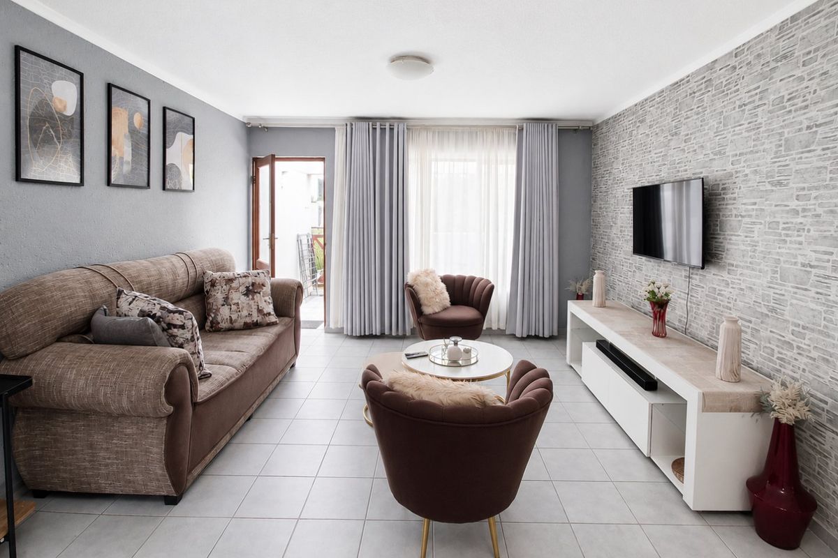A well-maintained living room featuring tiled flooring, a textured feature wall, and direct access to an outdoor balcony area.