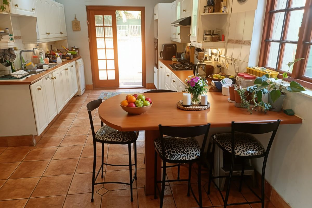 A functional kitchen featuring white cabinetry, gas hob, built-in oven, and tiled flooring, with an integrated breakfast bar and direct access to the rear exterior.
