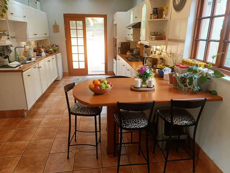 A functional kitchen featuring white cabinetry, gas hob, built-in oven, and tiled flooring, with an integrated breakfast bar and direct access to the rear exterior.