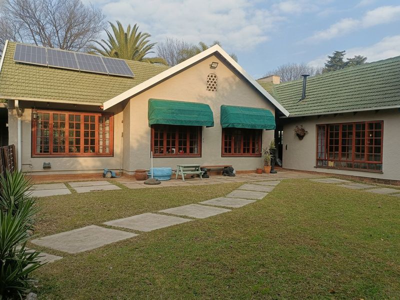 Rear view of the house featuring a paved patio area, lawn, timber-framed windows, and roof-mounted solar panels.
