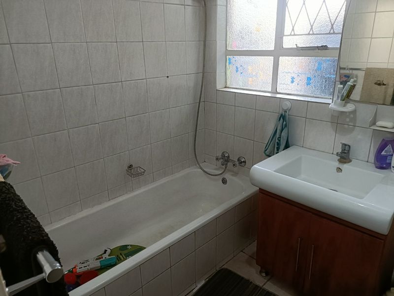 A functional bathroom featuring a bathtub with shower mixer, a vanity cabinet with basin, and tiled wall finishes.
