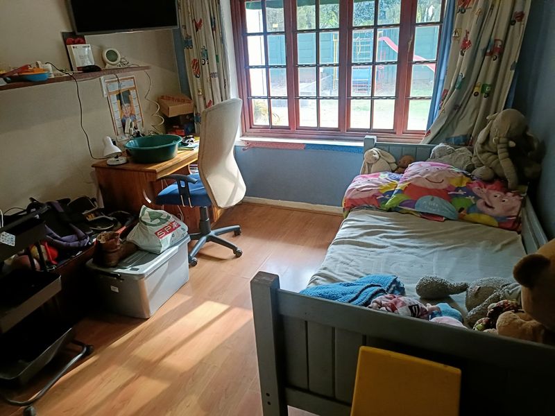 A functional bedroom featuring laminate flooring and a large timber-framed window providing natural light.