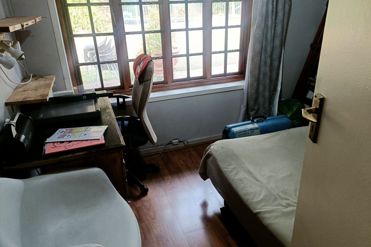 A compact bedroom featuring laminate flooring and a large timber-framed window providing natural light.