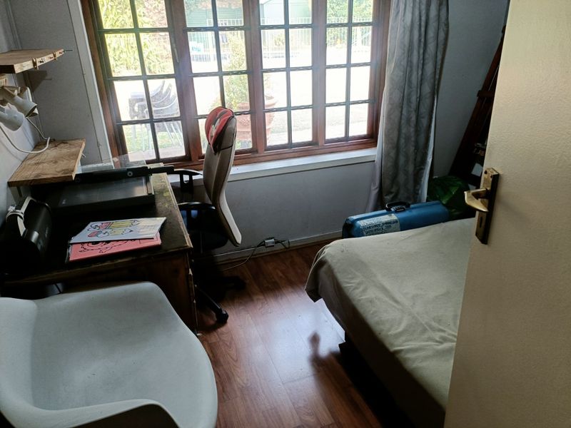 A compact bedroom featuring laminate flooring and a large timber-framed window providing natural light.