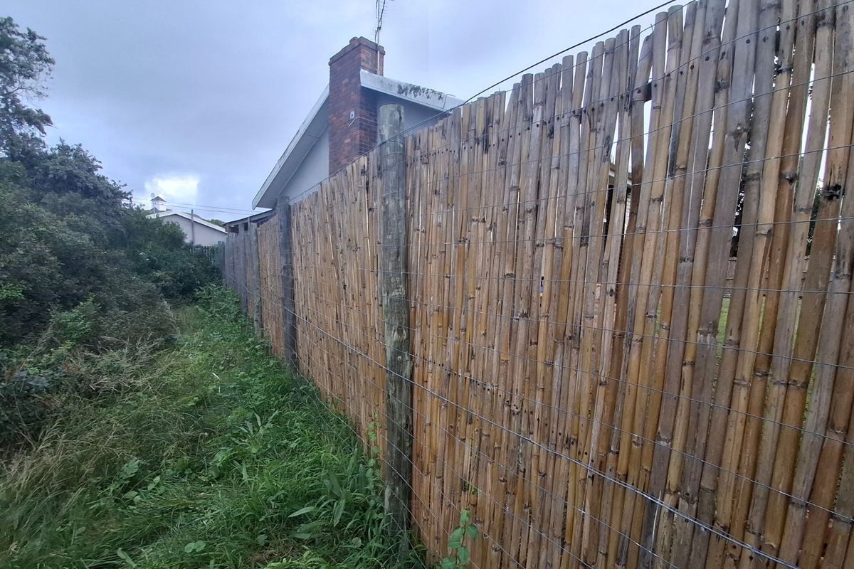 A view of the rear property boundary featuring a bamboo privacy fence, timber posts, and an adjacent brick chimney.