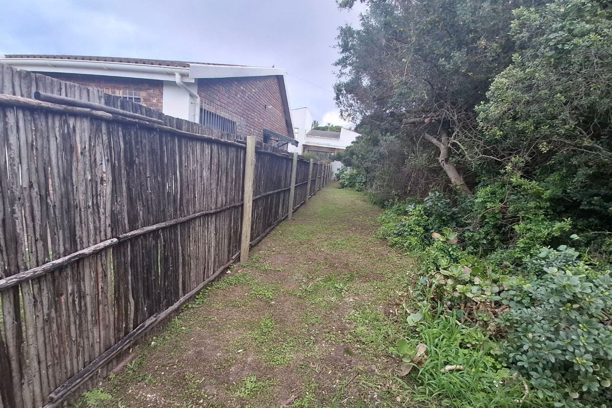 A side garden path featuring a weathered wooden pole fence bordering the property with established trees and shrubs.