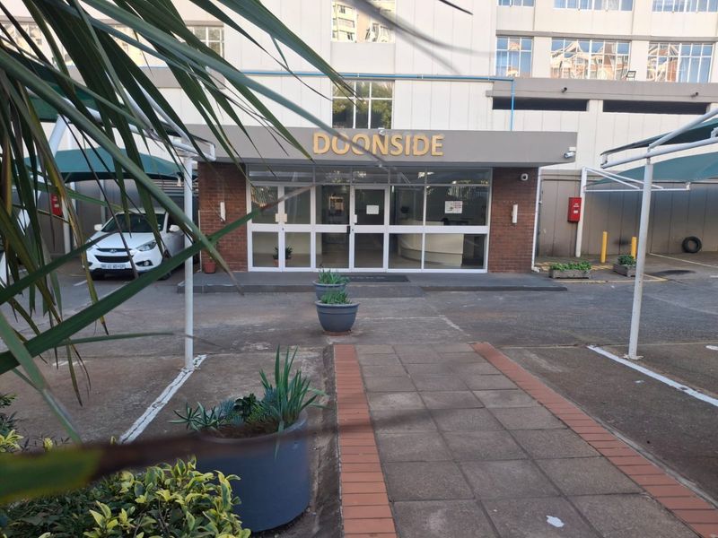 Front entrance view of Doonside apartment building featuring a paved driveway, covered parking areas, and a glass-fronted lobby entrance.