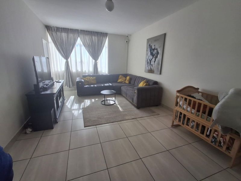 A spacious living room featuring neutral tiled flooring and a large window that allows for ample natural light.