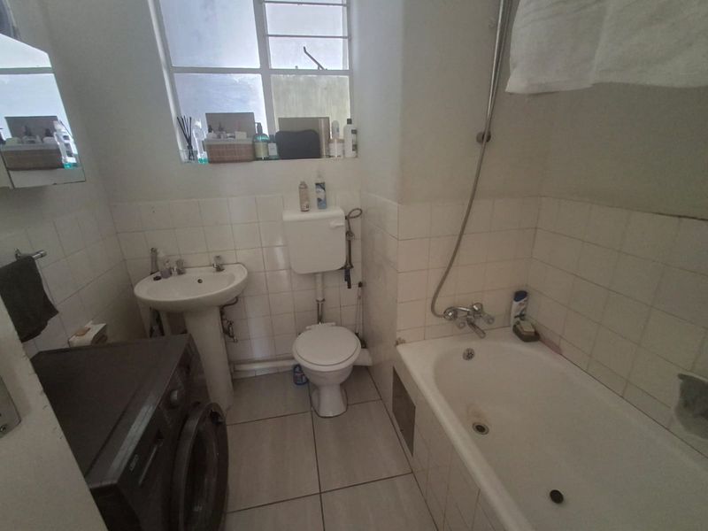 A functional bathroom featuring a pedestal basin, toilet, and bathtub with shower mixer, finished with tiled walls and flooring.