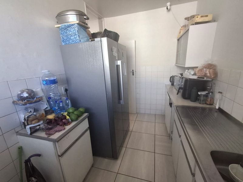 A compact kitchen featuring tiled walls, tiled flooring, built-in cabinetry, and a stainless steel sink, offering a functional layout for daily use.