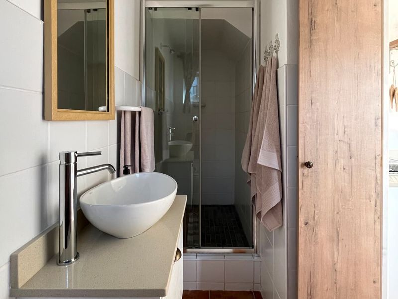 A modern bathroom featuring a vessel sink on a stone vanity, a framed mirror, and a glass-enclosed shower with tiled finishes.