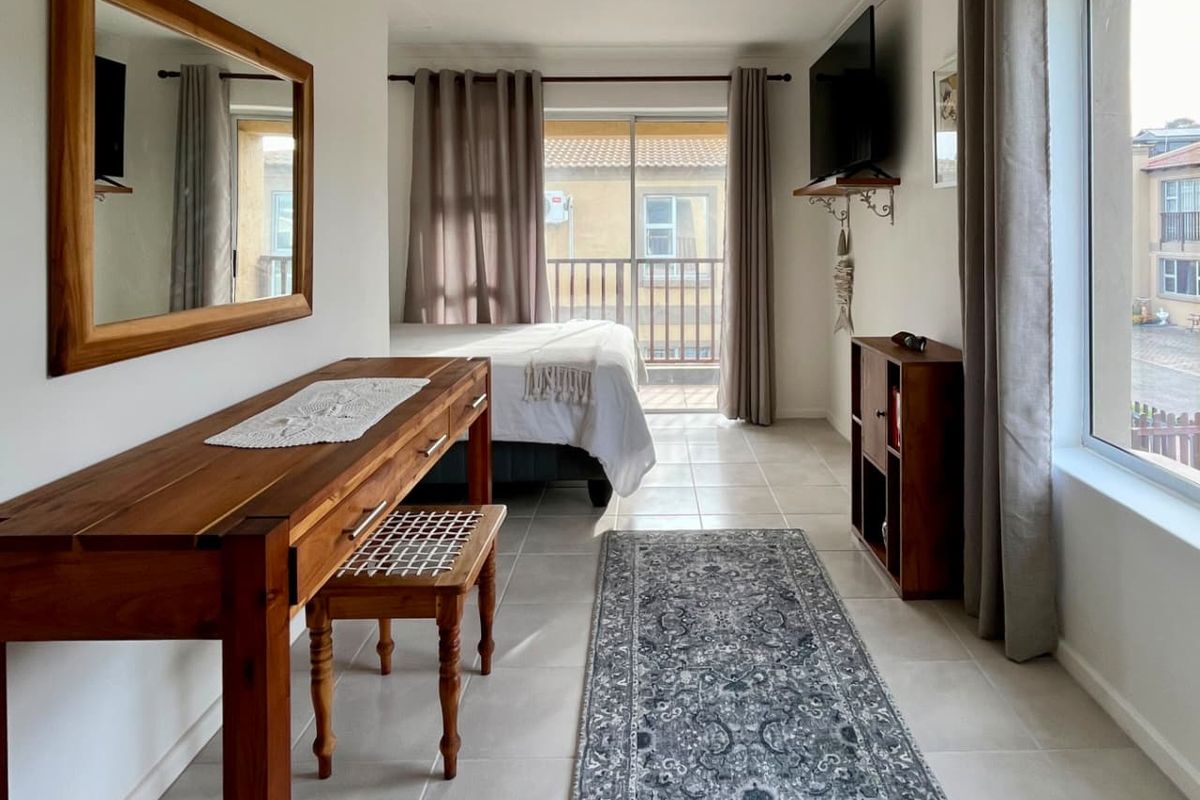 A bright bedroom featuring tiled flooring, a large window, and a sliding glass door providing direct access to a private balcony.