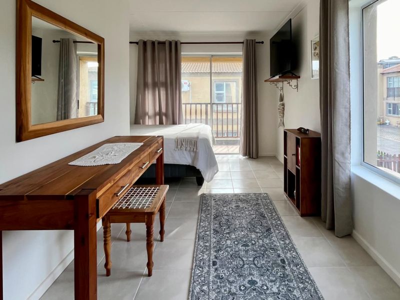 A bright bedroom featuring tiled flooring, a large window, and a sliding glass door providing direct access to a private balcony.