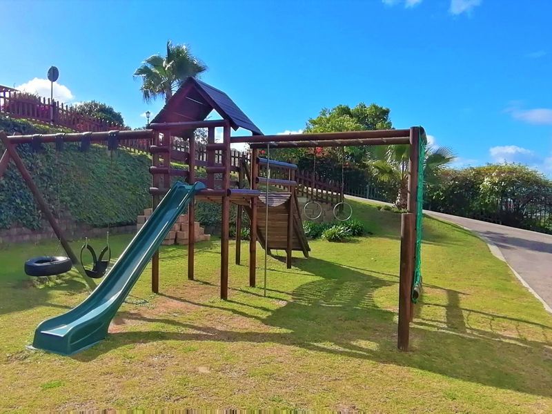A well-maintained communal garden area featuring a wooden playground structure with a slide and swings, set against a landscaped retaining wall.