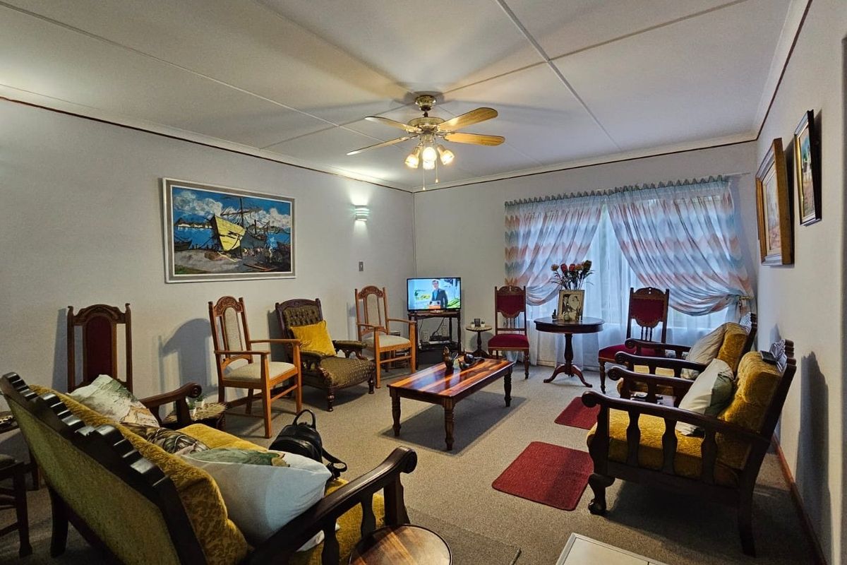 A traditional living room featuring a ceiling fan, wall sconces, and carpeted flooring, offering a comfortable and classic living space.