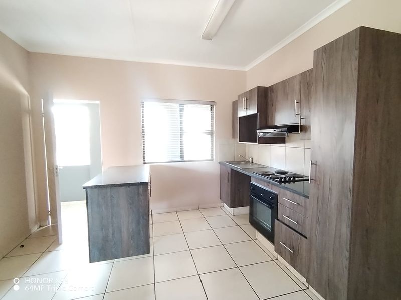 A functional kitchen featuring dark wood-look cabinetry, built-in oven and hob, a central island, and tiled flooring with access to an adjacent area.